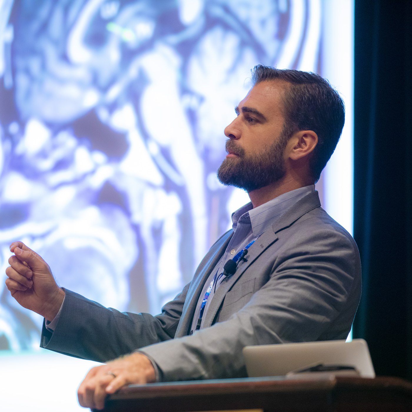 Dr. Chris Slininger presenting from a lectern with a brain MRI projected behind him